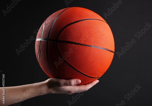 Basketball in woman hand on black background © Africa Studio