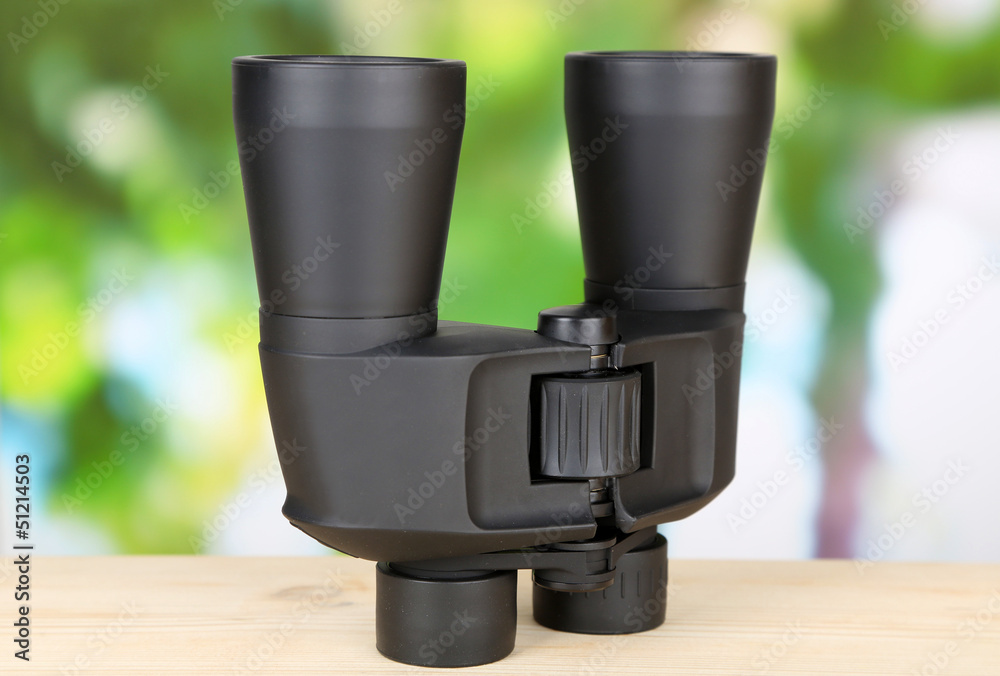 Black modern binoculars on wooden table on green background Black modern binoculars on wooden table on green background