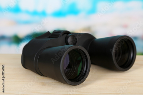 Black modern binoculars on wooden table on blue background