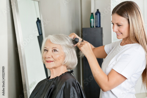 Hairstylist Straightening Woman's Hair At Salon