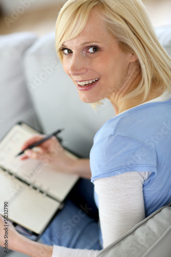 Blond woman in couch writing on agenda