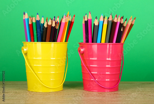 Colorful pencils in two pails on table on green background