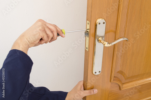 Carpenter fixing a lock in the door  with a screwdriver photo
