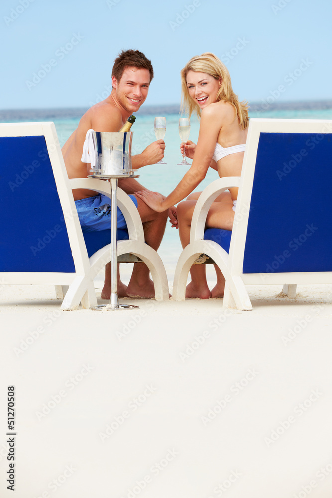 Couple On Beach Relaxing In Chairs And Drinking Champagne