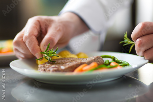 Chef hands decorating a dish in restaurant kitchen
