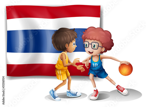 Two boys playing basketball in front of the Thailand flag