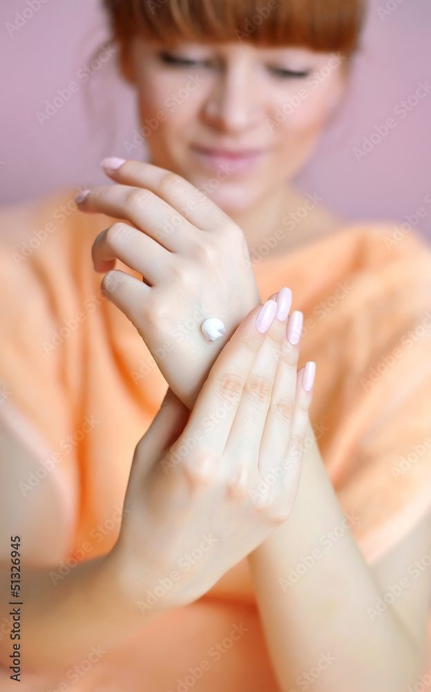 Young woman applies cream on her hands after bath. Focus on hand