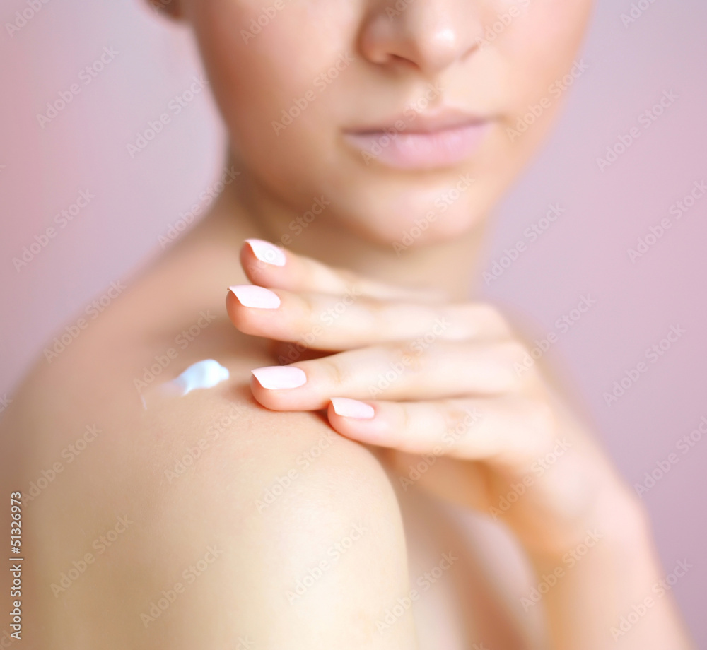 Young woman with cream on her shoulder. Focus is on a hand