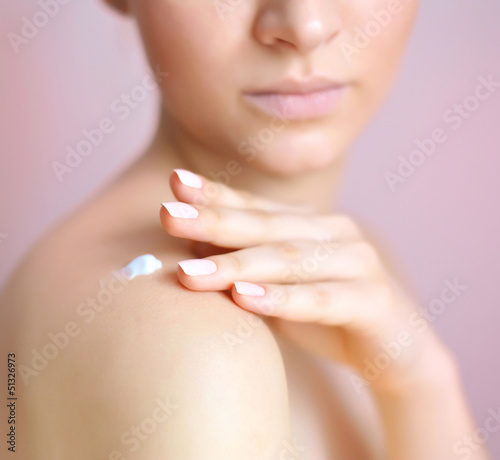 Young woman with cream on her shoulder. Focus is on a hand