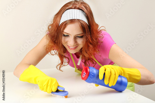 Young housewife cleaning up table at home on grey background