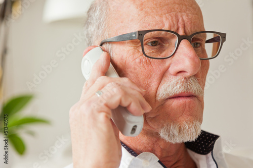 Senior man calling with portable phone in living room.