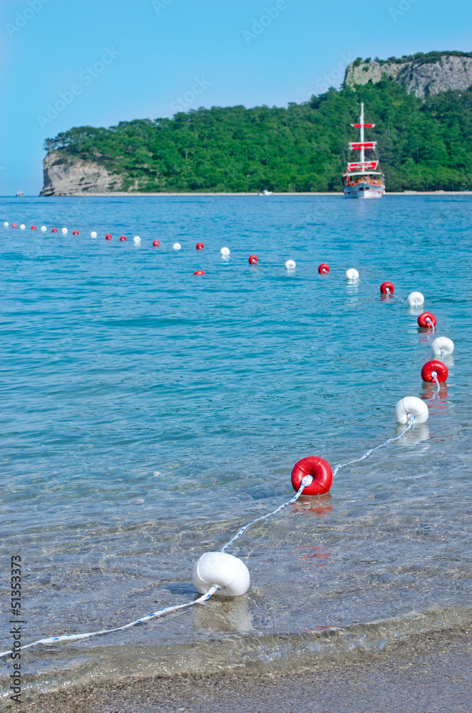Red and white buoys and a ship with red sails. Kemer, Antalya