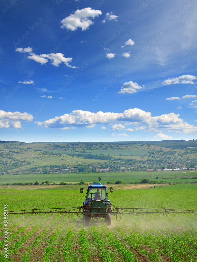 Fototapeta premium Farming tractor plowing and spraying on field vertical
