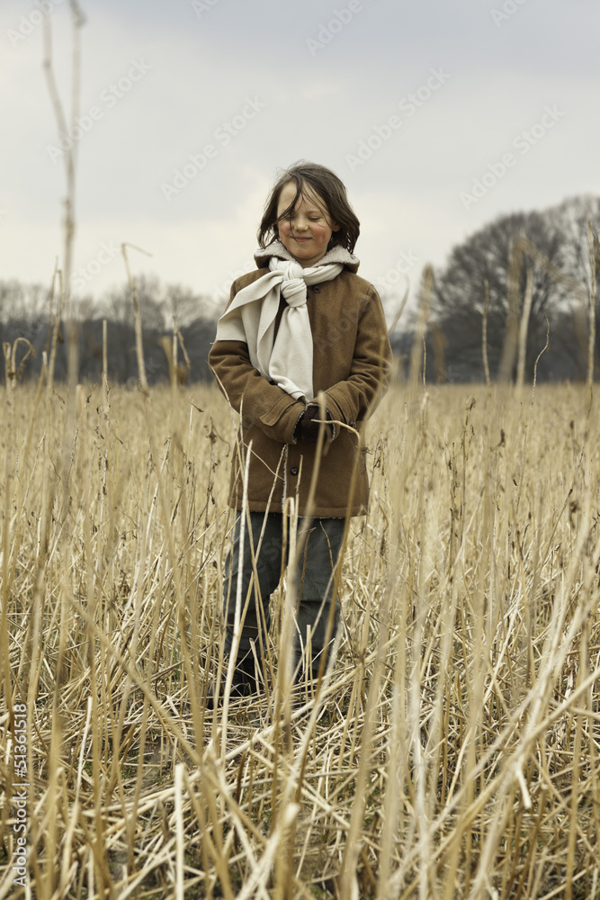 Playful funny young boy with long hair outdoor in wheat field.