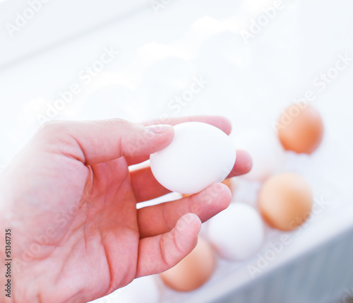 male hand holding white egg in front of package full of other eg