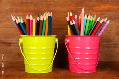 Colorful pencils in two pails on wooden background