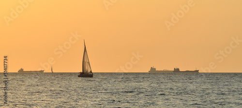 yacht sailing against huge cargo ship at the sunset photo