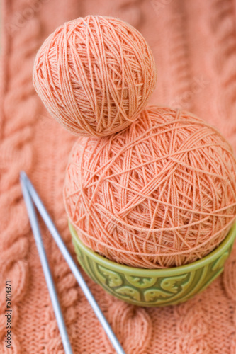 Two peach-colored ball of yarn are in plate and needles photo