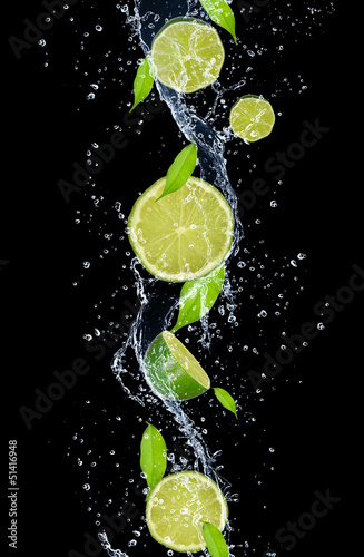 Limes in water splash, isolated on black background