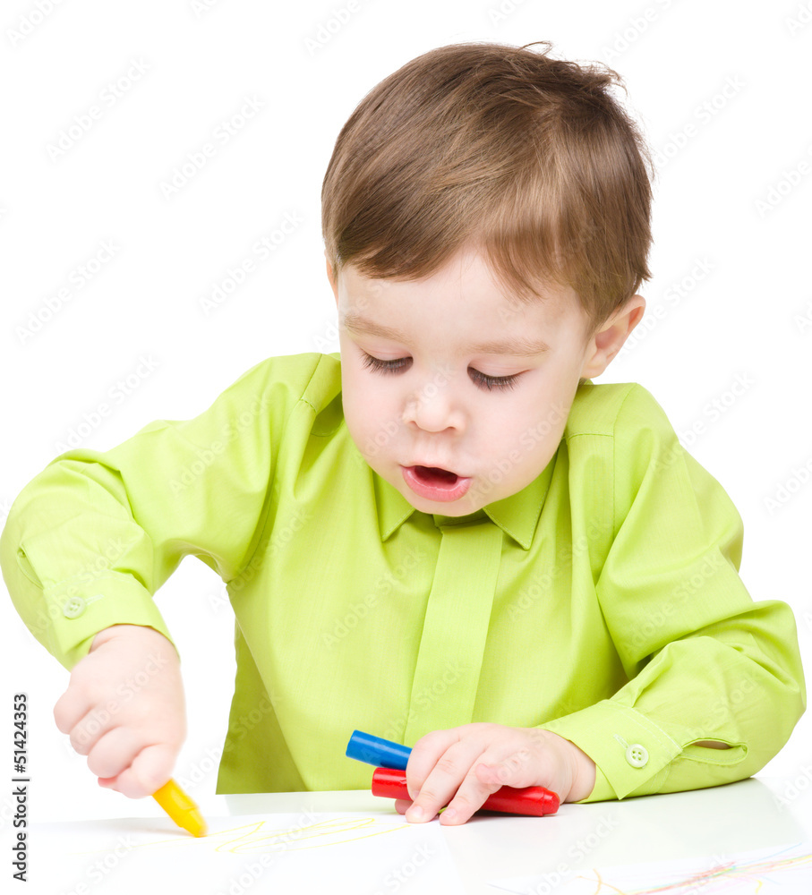 Little boy is drawing on white paper using crayon Little boy is drawing on white paper using crayon