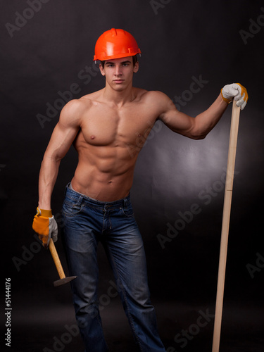 Muscular young worker with a hammer on a black background.