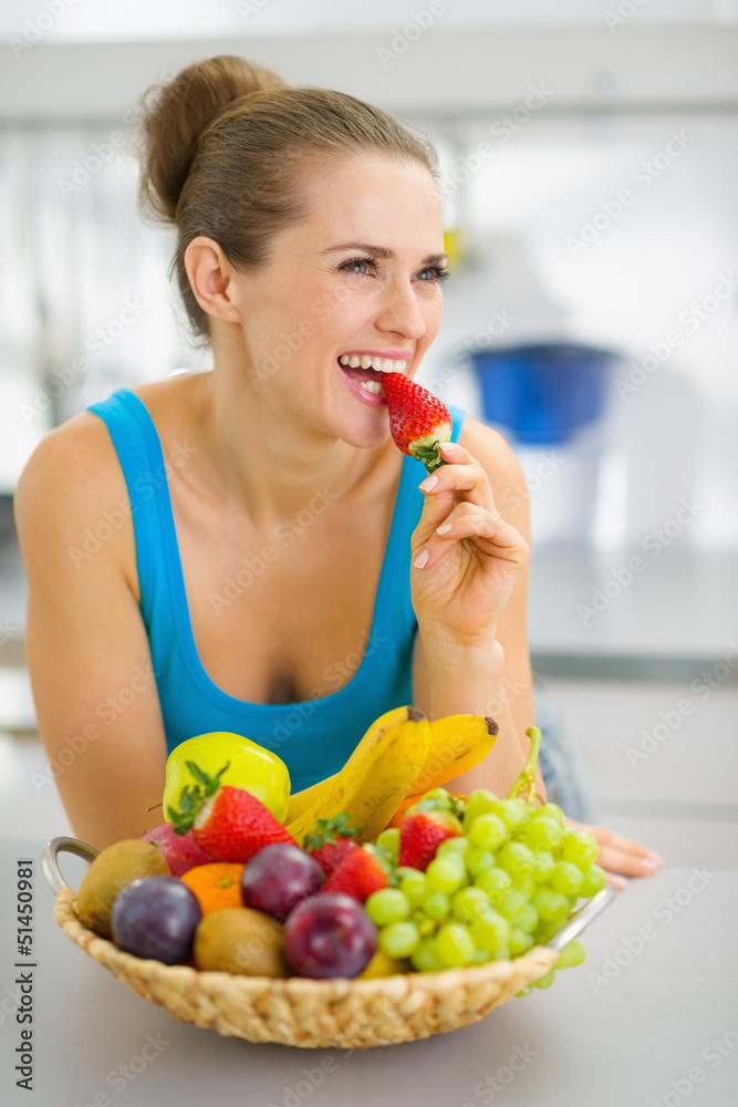 Happy young woman eating strawberry in modern kitchen Happy young woman eating strawberry in modern kitchen