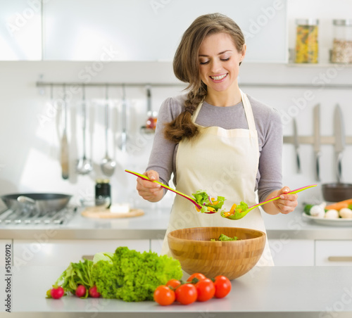 Smiling young housewife mixing fresh salad