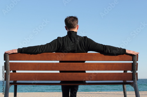 Dark dressed man relaxing on a bench in the sund