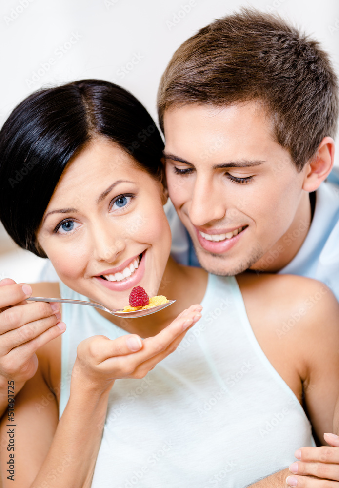 Young man feeds his girlfriend sitting at the kitchen table Young man feeds his girlfriend sitting at the kitchen table