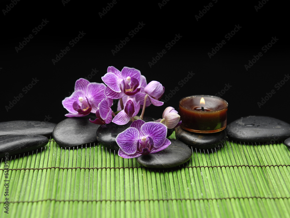 Branch orchid with black stones and candle on mat Branch orchid with black stones and candle on mat