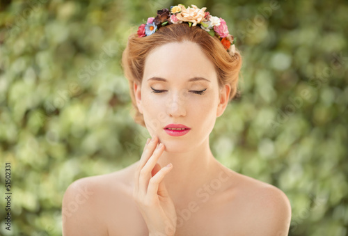 Beautiful young woman with flowers wreath in hair on natural gre
