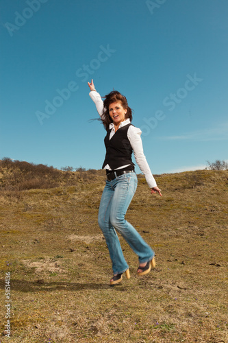 Happy pretty brunette woman wearing jeans in meadow with blue sk