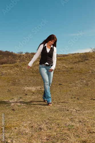 Happy pretty brunette woman wearing jeans in meadow with blue sk