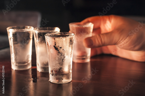 Shot glass of vodka in hand on a wooden table.