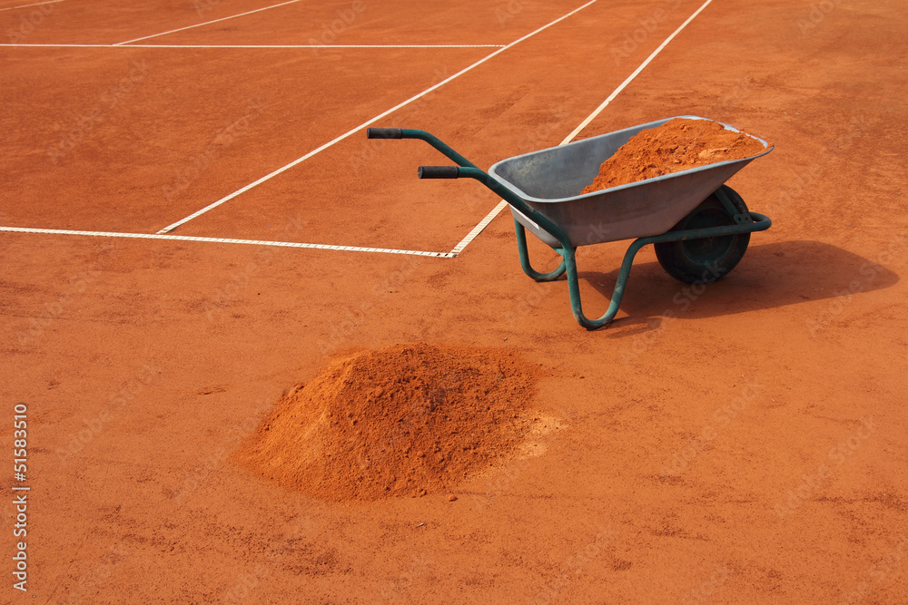 Fototapeta premium Wheelbarrow filled with red clay, on the tennis court