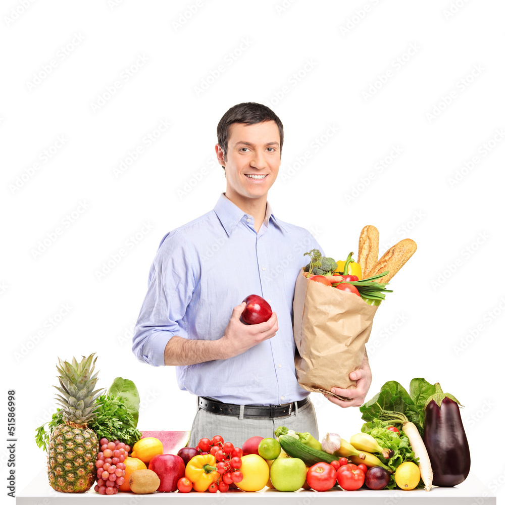 Smiling man holding an apple and bag with food products, posing