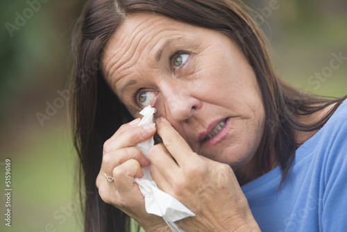 Sad mature woman tissue cleaning tears in eye