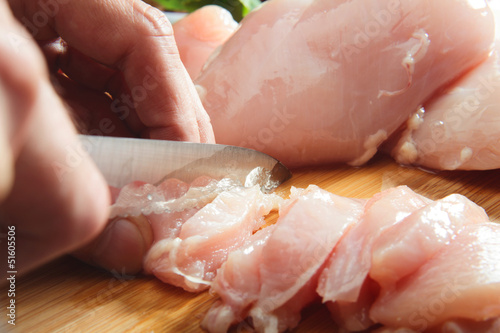 Man's hand cutting raw chicken breast