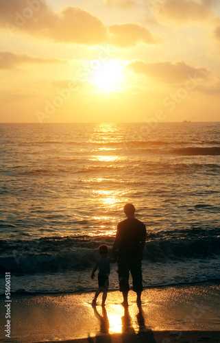 father and son on a walk by the sea at sunset