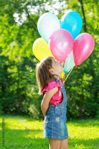 Little happy girl holding colorful balloons in green park
