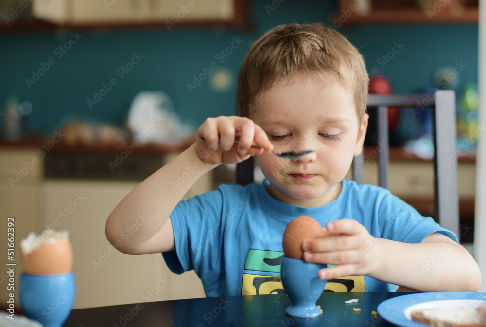 Small happy three year old boy breaks the egg