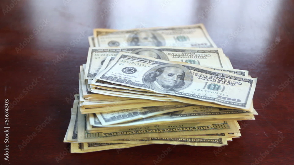 Hundred dollar bills falling into a stack on a table. Hundred dollar bills falling into a stack on a table.