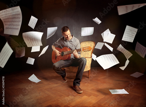 Young man playing guitar with sheet music flying around him