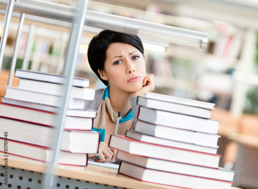 Sad female student is tired of education surrounded with books Sad female student is tired of education surrounded with books