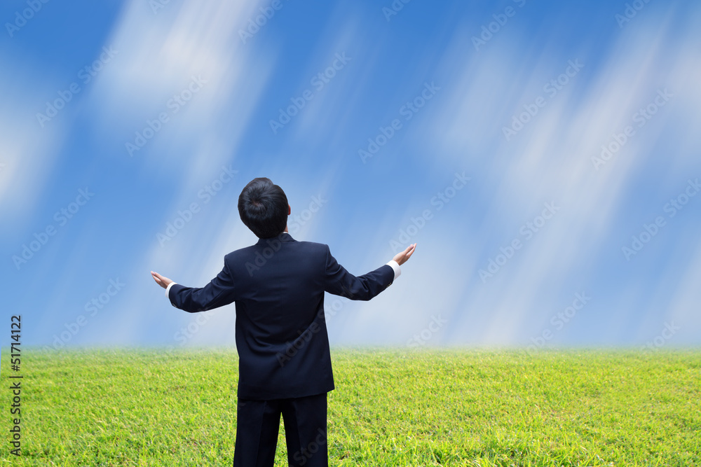 Young man standing on a meadow with raised hands and looking to Young man standing on a meadow with raised hands and looking to