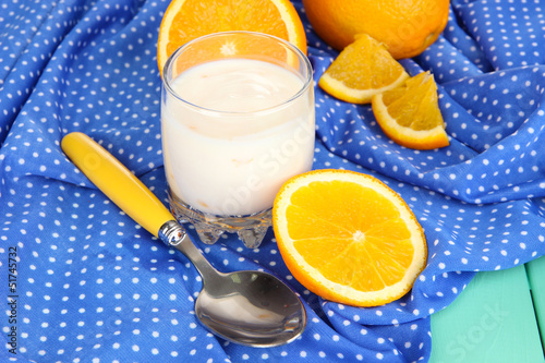 Delicious yogurt in glass with orange on blue tablecloth