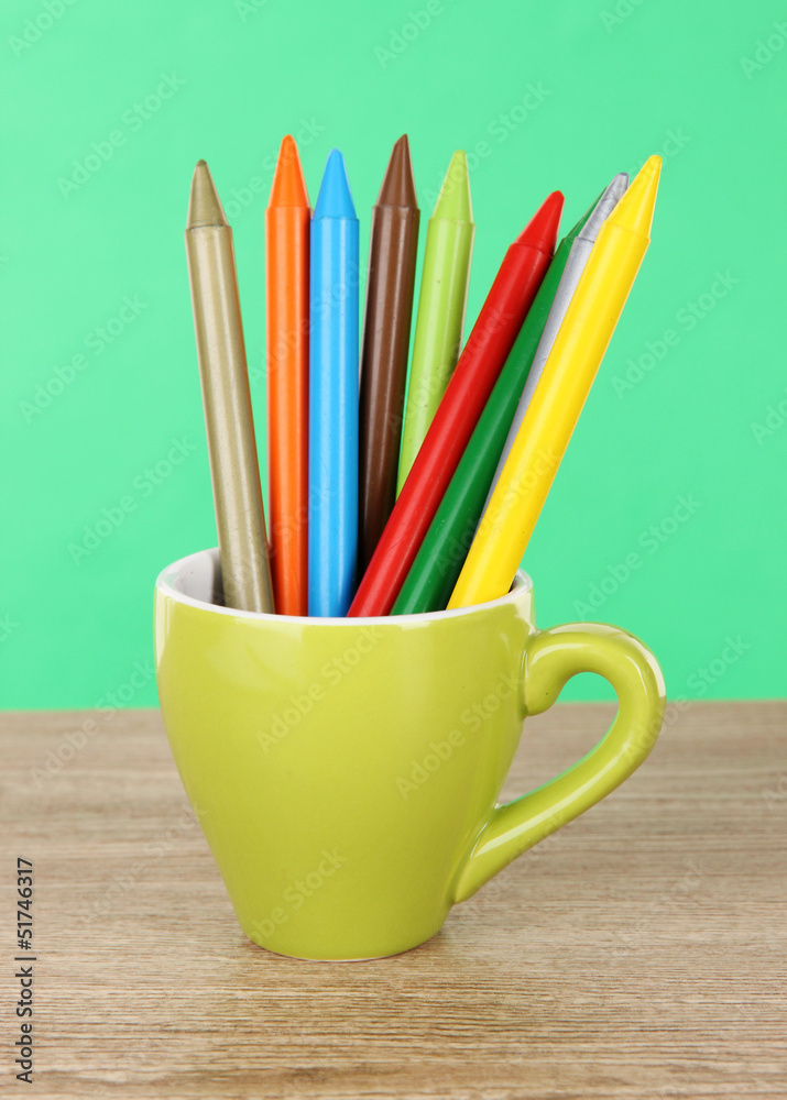 Colorful pencils in cup on table on green background Colorful pencils in cup on table on green background