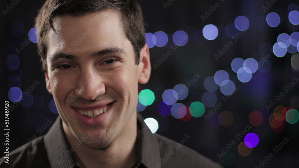 Young man looking at camera, smiling with lights in background Young man looking at camera, smiling with lights in background