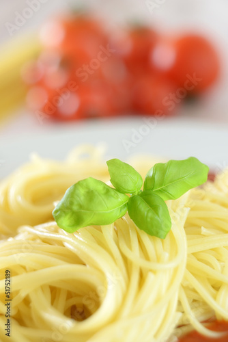 Spaghetti mit Basilikumblättern, Tomaten im Hintergrund
