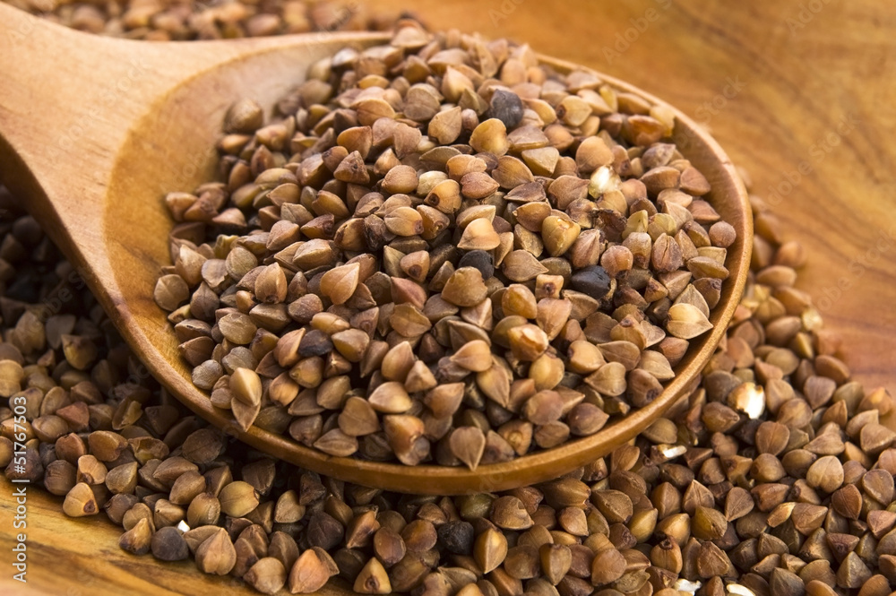 Fototapeta premium Buckwheat seeds on wooden spoon in closeup